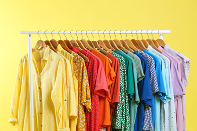 Bright clothes hanging on rack against yellow background. Rainbow colors