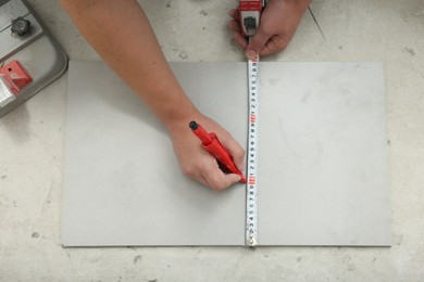 Photo of Worker measuring and marking ceramic tile on floor, closeup