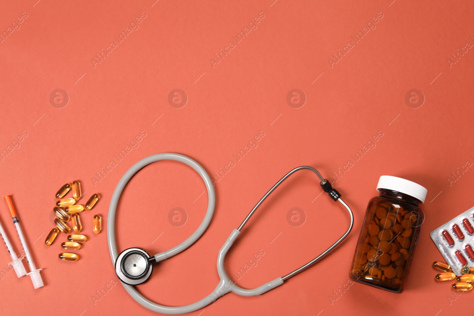 Photo of Stethoscope, syringes and pills on crimson background, flat lay. Space for text