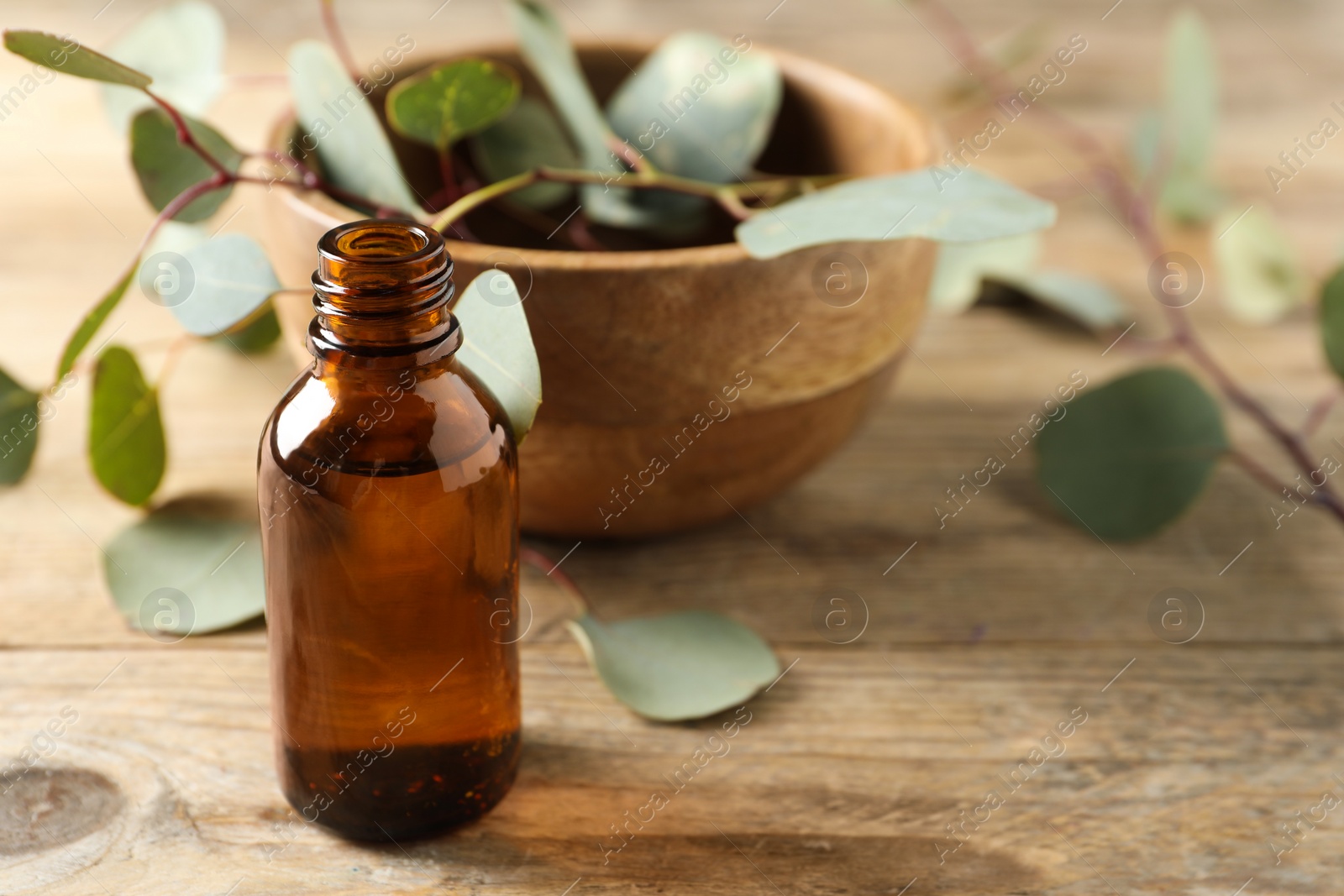 Photo of Bottle of eucalyptus essential oil and leaves on wooden table. Space for text