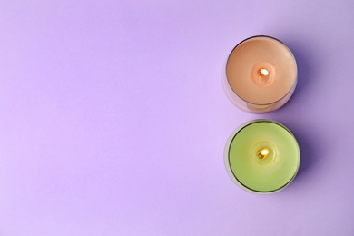 Photo of Burning wax candles in glass holders on purple background, flat lay. Space for text
