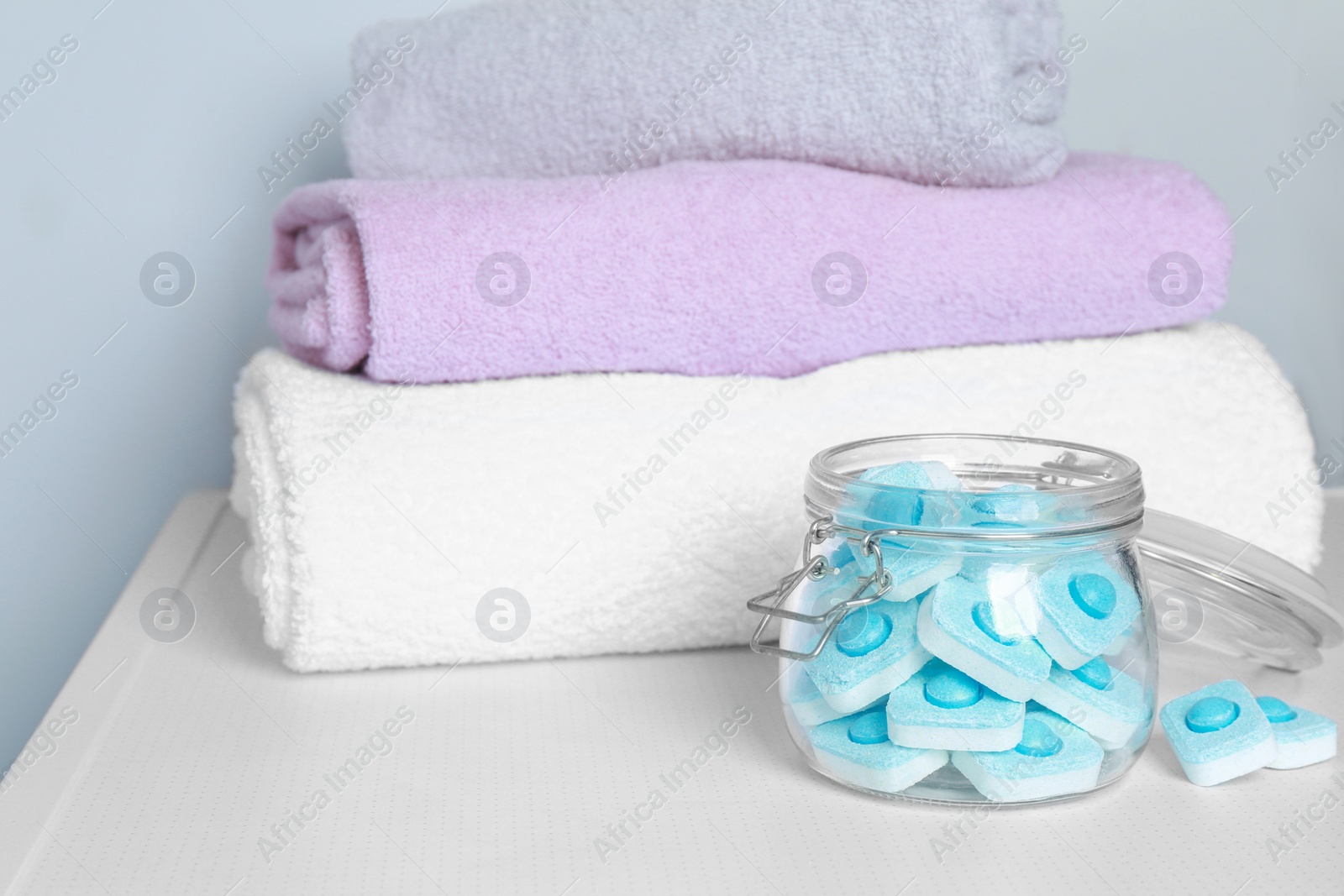 Photo of Jar with water softener tablets near stacked towels on white table