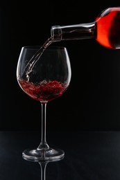 Photo of Pouring red wine from bottle into glass on black background