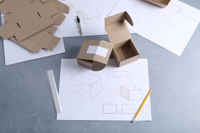 Photo of Creating packaging design. Drawings, boxes and stationery on blue textured table, flat lay