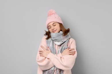 Beautiful woman in warm scarf and hat on gray background