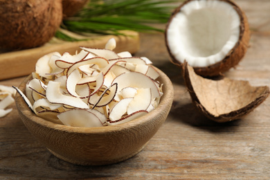 Photo of Tasty coconut chips in bowl on wooden table