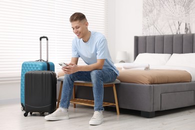 Smiling guest with smartphone and suitcase in stylish hotel room