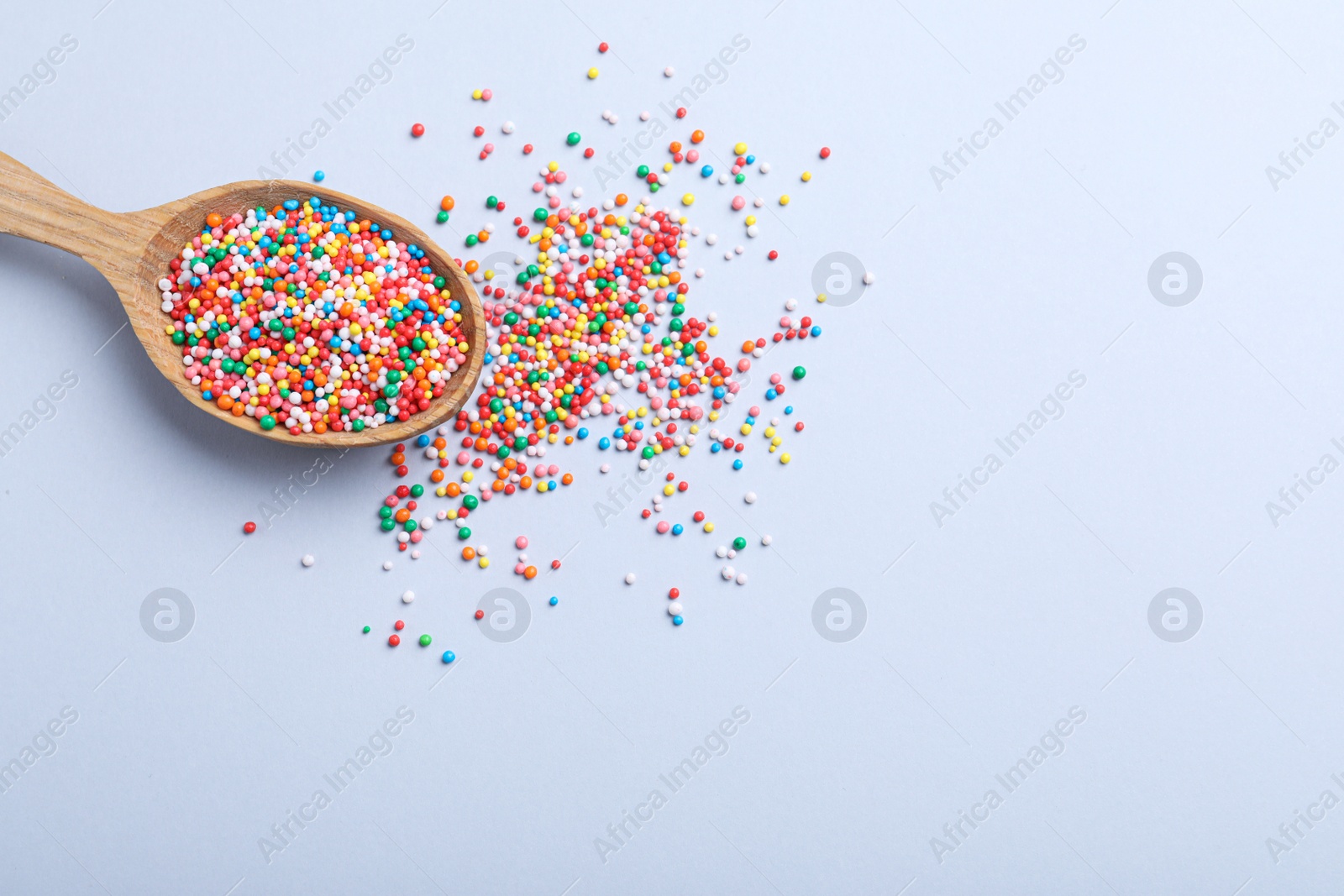 Photo of Colorful sprinkles in spoon on light grey background, flat lay with space for text. Confectionery decor