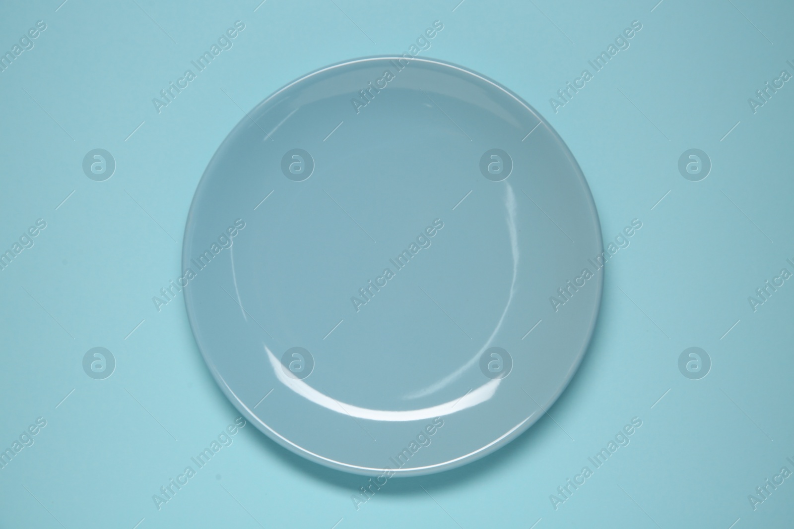 Photo of One ceramic plate on light blue background, top view