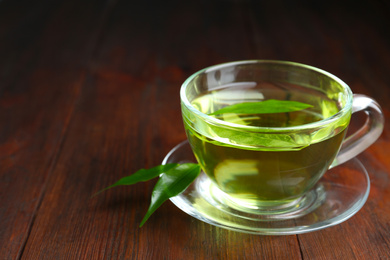 Cup of aromatic green tea and leaves on wooden table