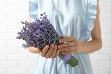 Photo of Woman holding fresh lavender flowers against white brick wall, closeup view