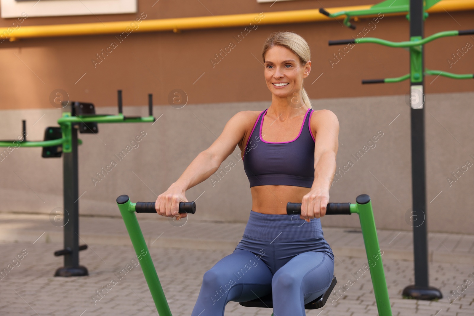 Photo of Happy woman training on rowing machine at outdoor gym