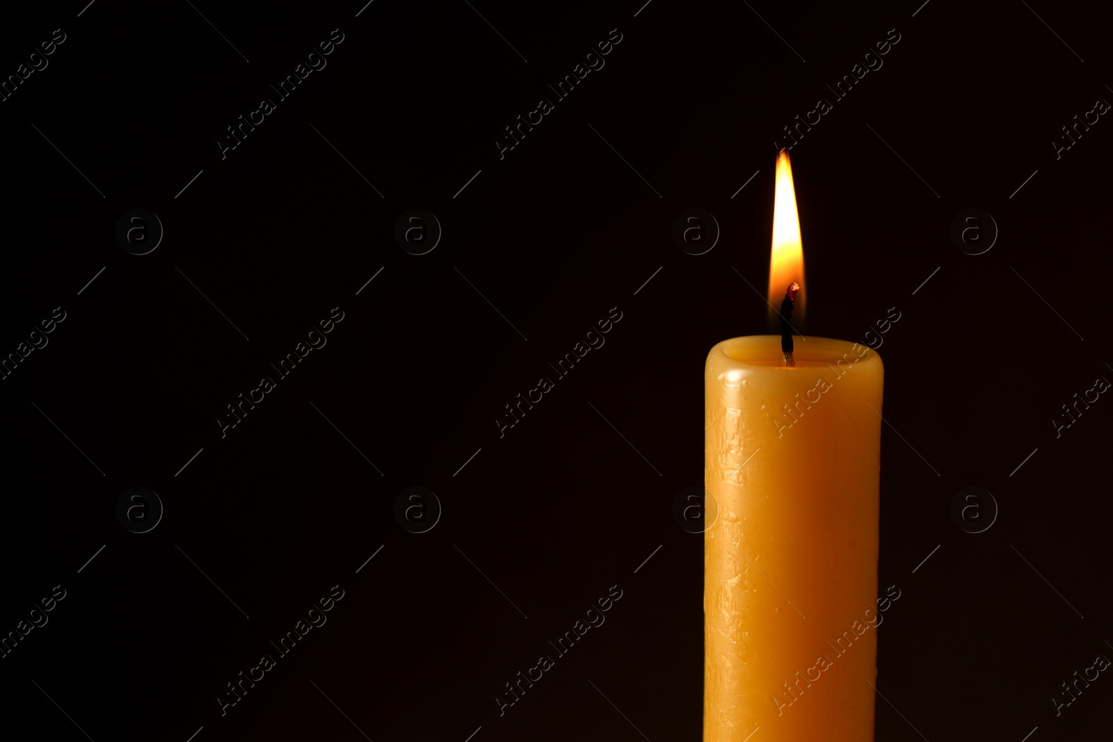 Photo of Burning church wax candle on dark background, closeup. Space for text