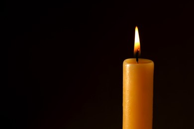 Photo of Burning church wax candle on dark background, closeup. Space for text