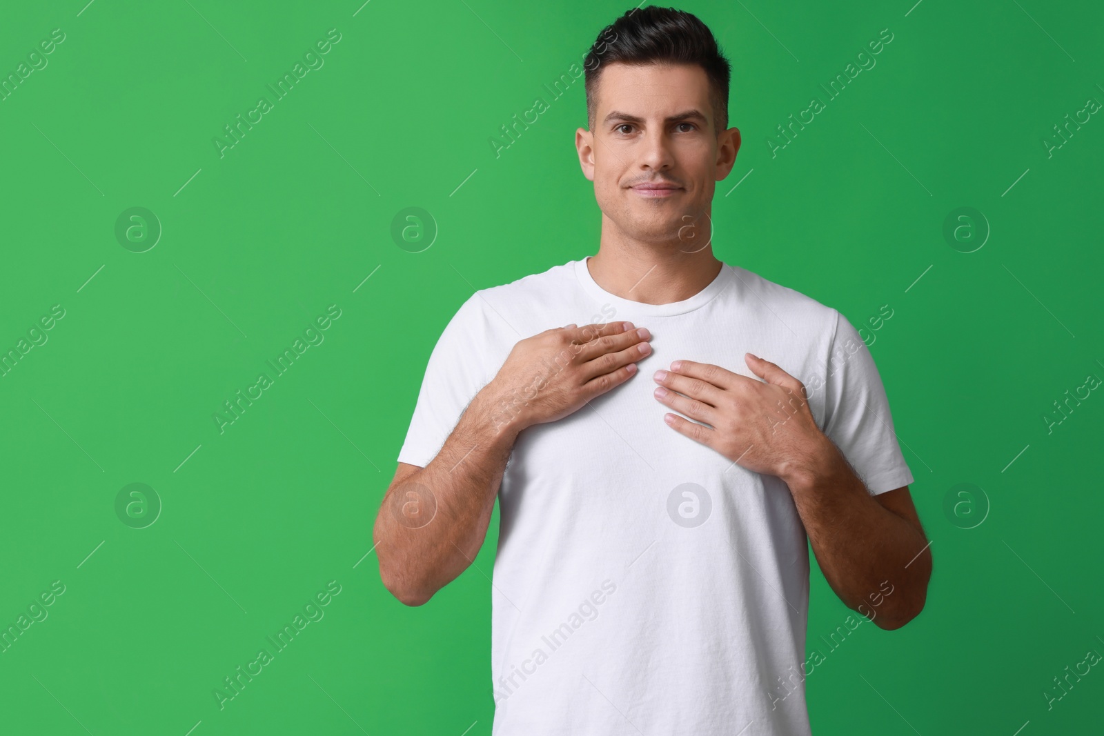 Photo of Handsome man holding hands near chest on green background. Space for text