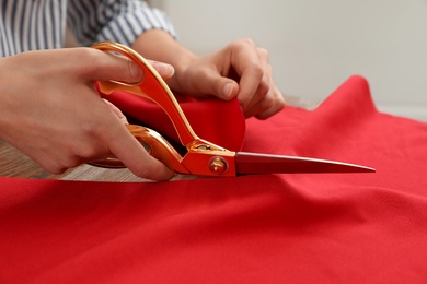 Woman cutting fabric with sharp scissors at wooden table, closeup