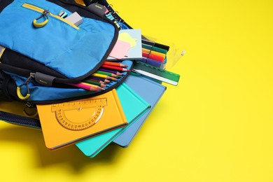 Photo of Backpack with school stationery on yellow background, space for text