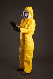 Photo of Woman in chemical protective suit holding clipboard on grey background. Virus research