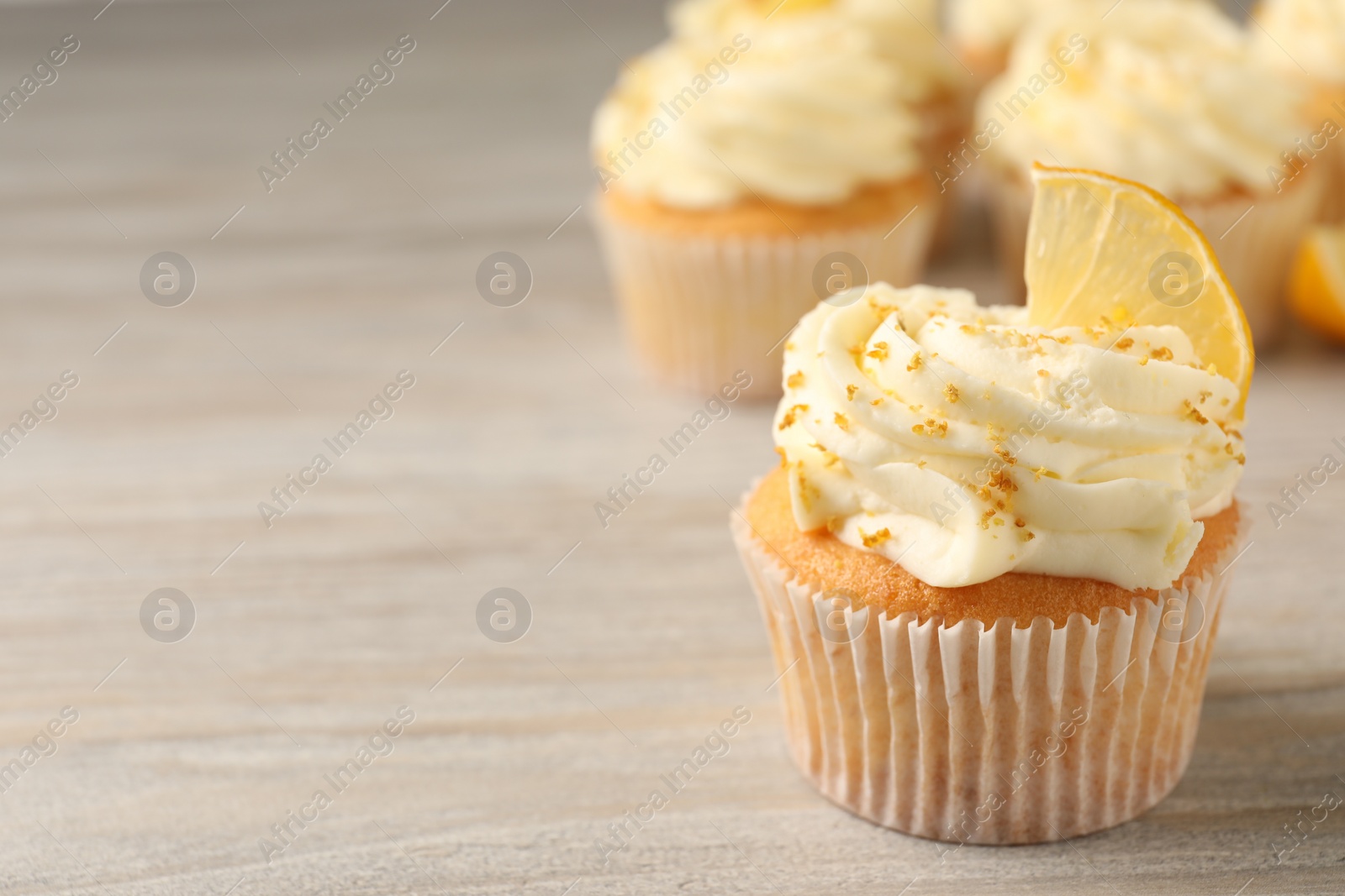 Photo of Tasty cupcake with cream, zest and lemon slice on light wooden table, closeup. Space for text