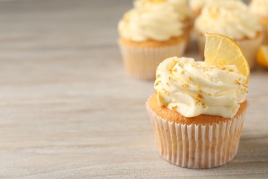 Tasty cupcake with cream, zest and lemon slice on light wooden table, closeup. Space for text