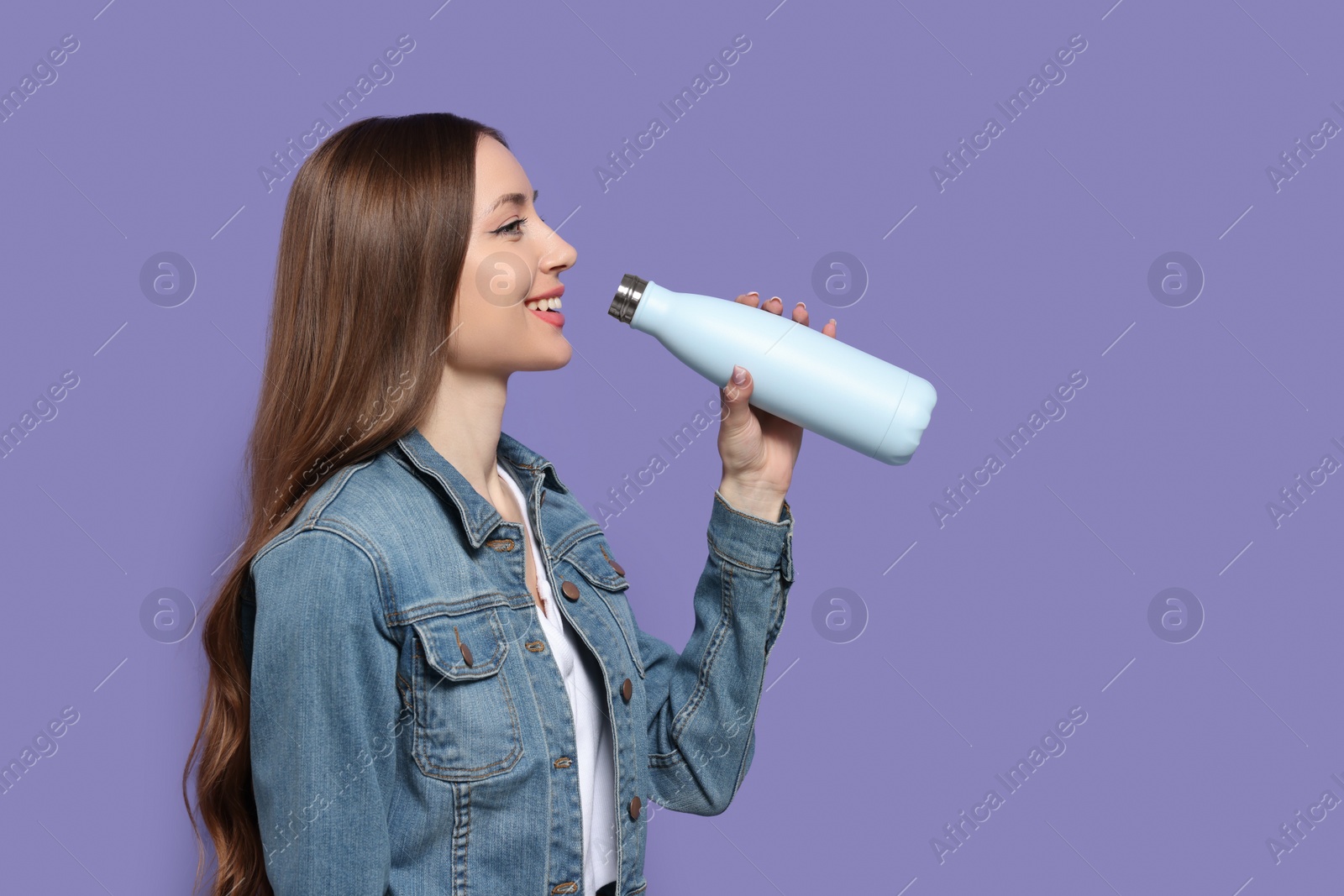 Photo of Beautiful young woman with thermos bottle on purple background