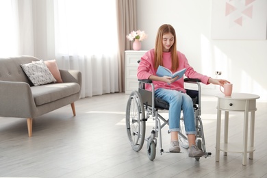 Teenage girl with book and drink in wheelchair at home