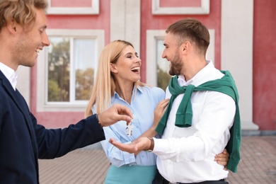 Photo of Male real estate agent giving house key to couple outdoors