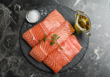 Photo of Top view of fresh raw salmon with parsley, oil and salt on black marble table. Fish delicacy