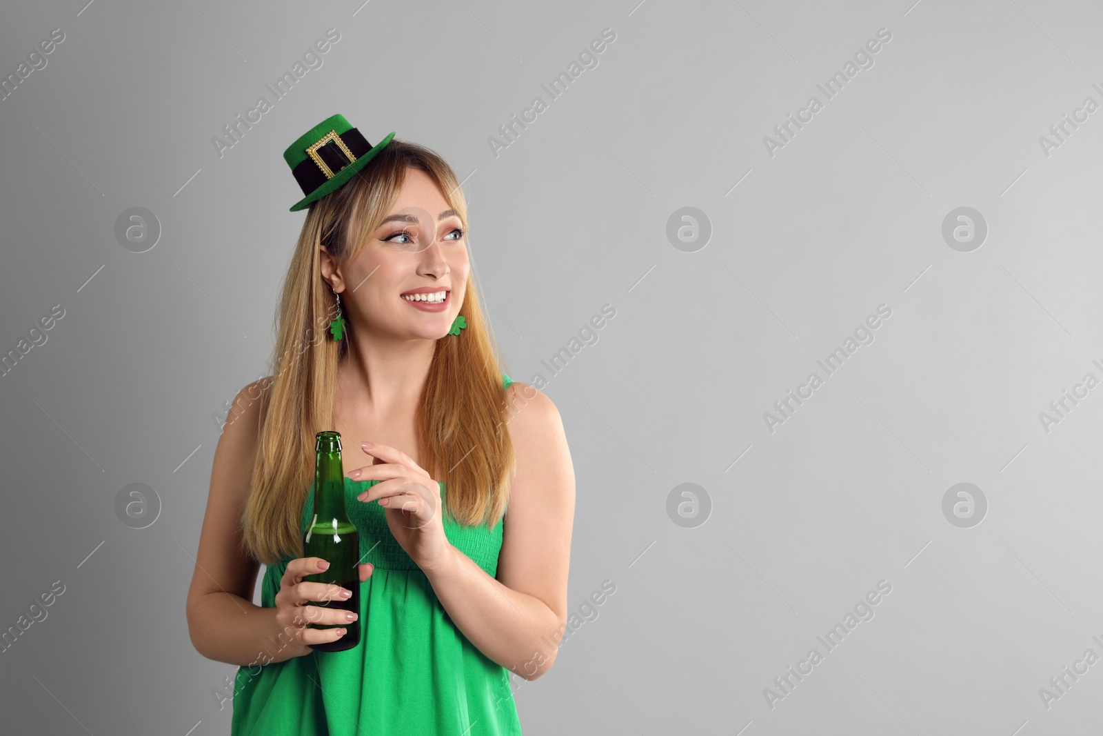 Photo of Happy woman in St Patrick's Day outfit with beer on light grey background, space for text