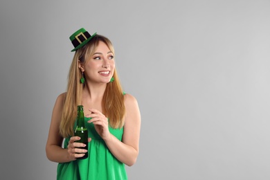 Happy woman in St Patrick's Day outfit with beer on light grey background, space for text