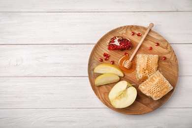 Flat lay composition with honey, dipper, sliced apples and pomegranate on wooden background. Rosh Hashanah holiday