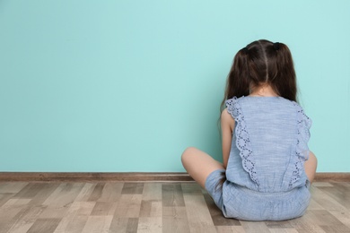Little girl sitting on floor near color wall in empty room. Autism concept