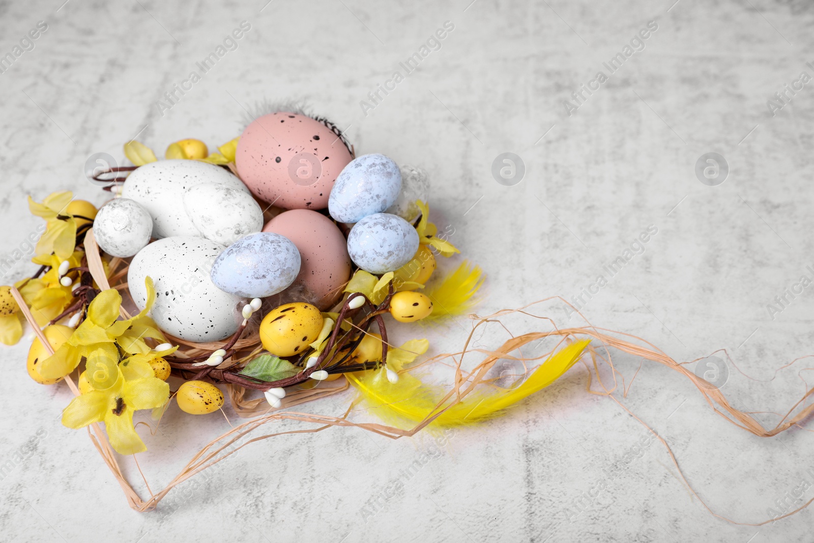 Photo of Decorative nest with many painted Easter eggs on light textured background
