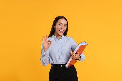 Photo of Happy woman with folder showing OK gesture on orange background