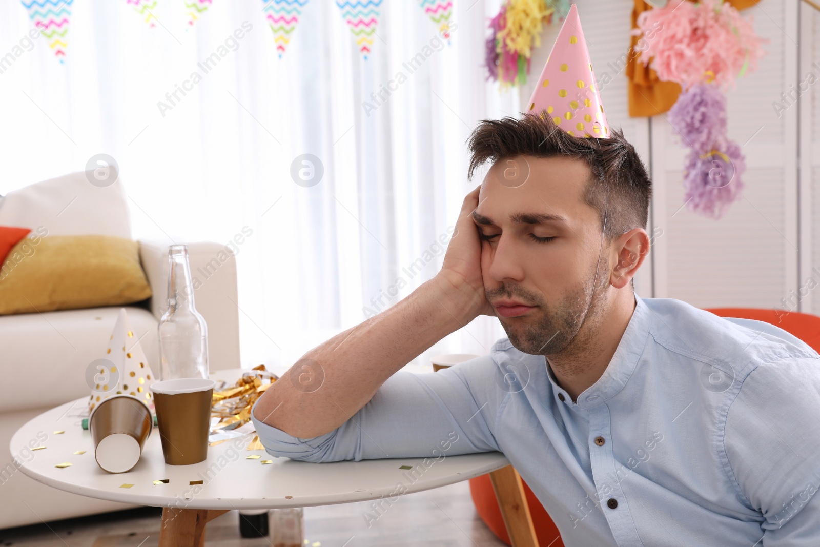 Photo of Young man suffering from hangover in room after party