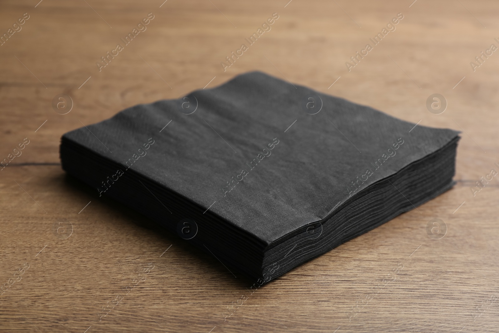 Photo of Stack of black clean paper tissues on wooden table