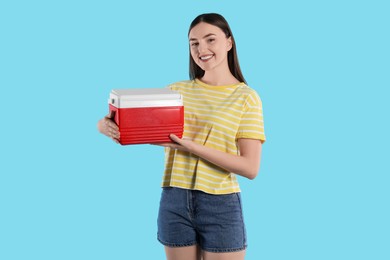 Photo of Happy young woman with plastic cool box on light blue background