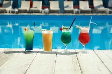 Refreshing cocktails on wooden deck near swimming pool outdoors