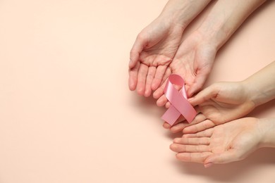 Photo of Breast cancer awareness. Women holding pink ribbon on beige background, top view. Space for text