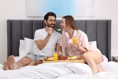 Photo of Healthy breakfast. Happy husband feeding his wife on bed at home