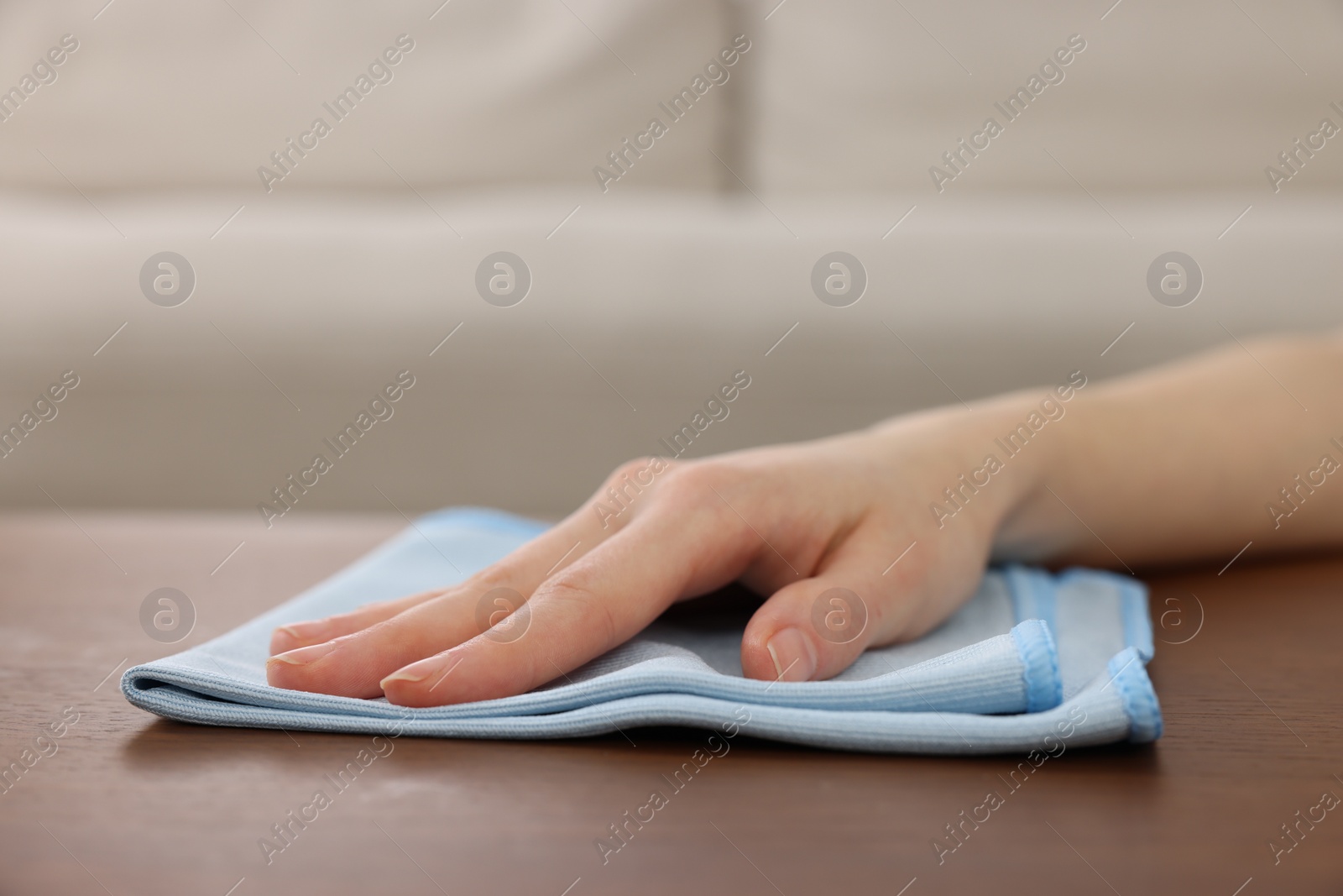 Photo of Woman with microfiber cloth cleaning wooden table in room, closeup. Space for text