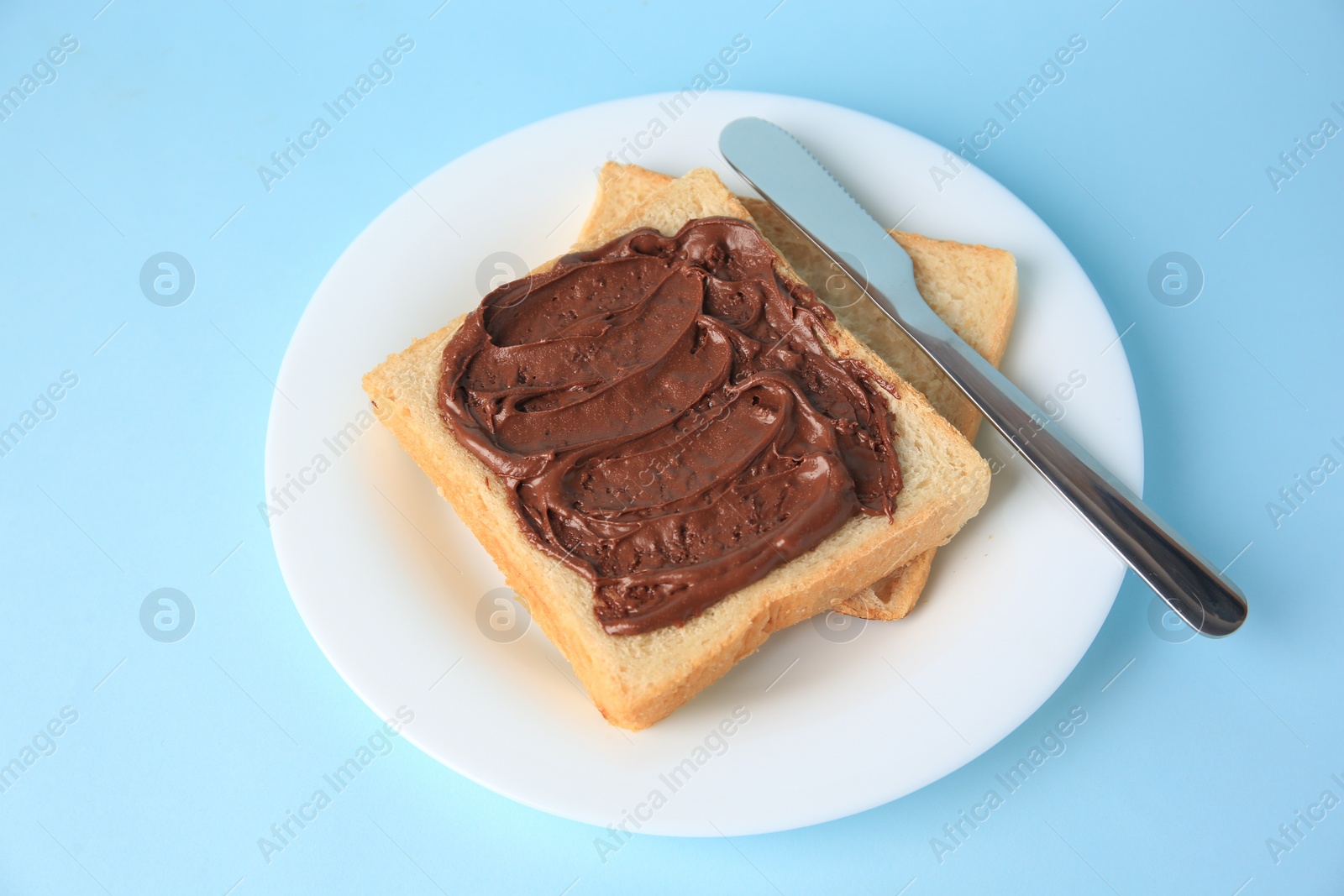 Photo of Tasty toast with chocolate paste on light blue background