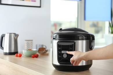 Woman turning on modern electric multi cooker in kitchen. Space for text