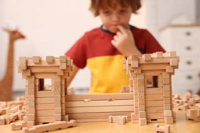 Photo of Little boy playing with wooden construction set at table in room, selective focus. Child's toy