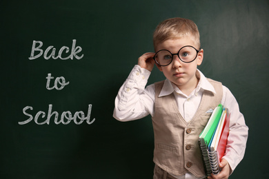 Image of Cute little child wearing glasses near chalkboard with phrase BACK TO SCHOOL