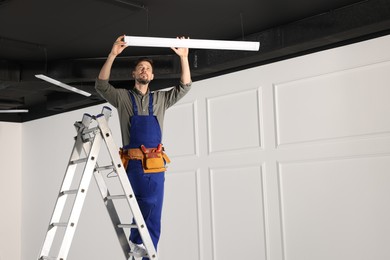 Photo of Electrician in uniform installing ceiling lamp indoors. Space for text