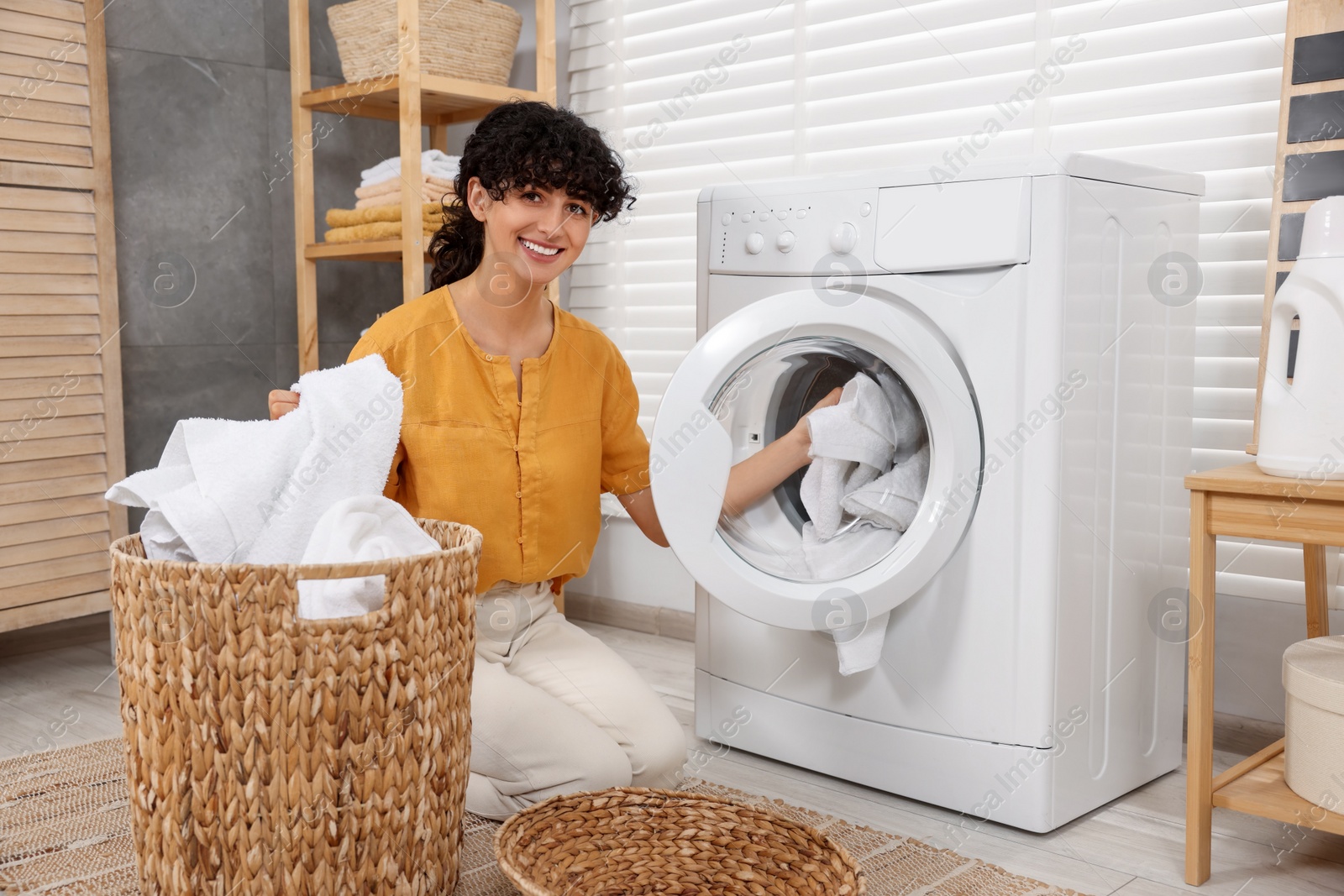 Photo of Happy woman putting laundry into washing machine indoors