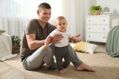 Photo of Father supporting his baby daughter while she learning to walk at home