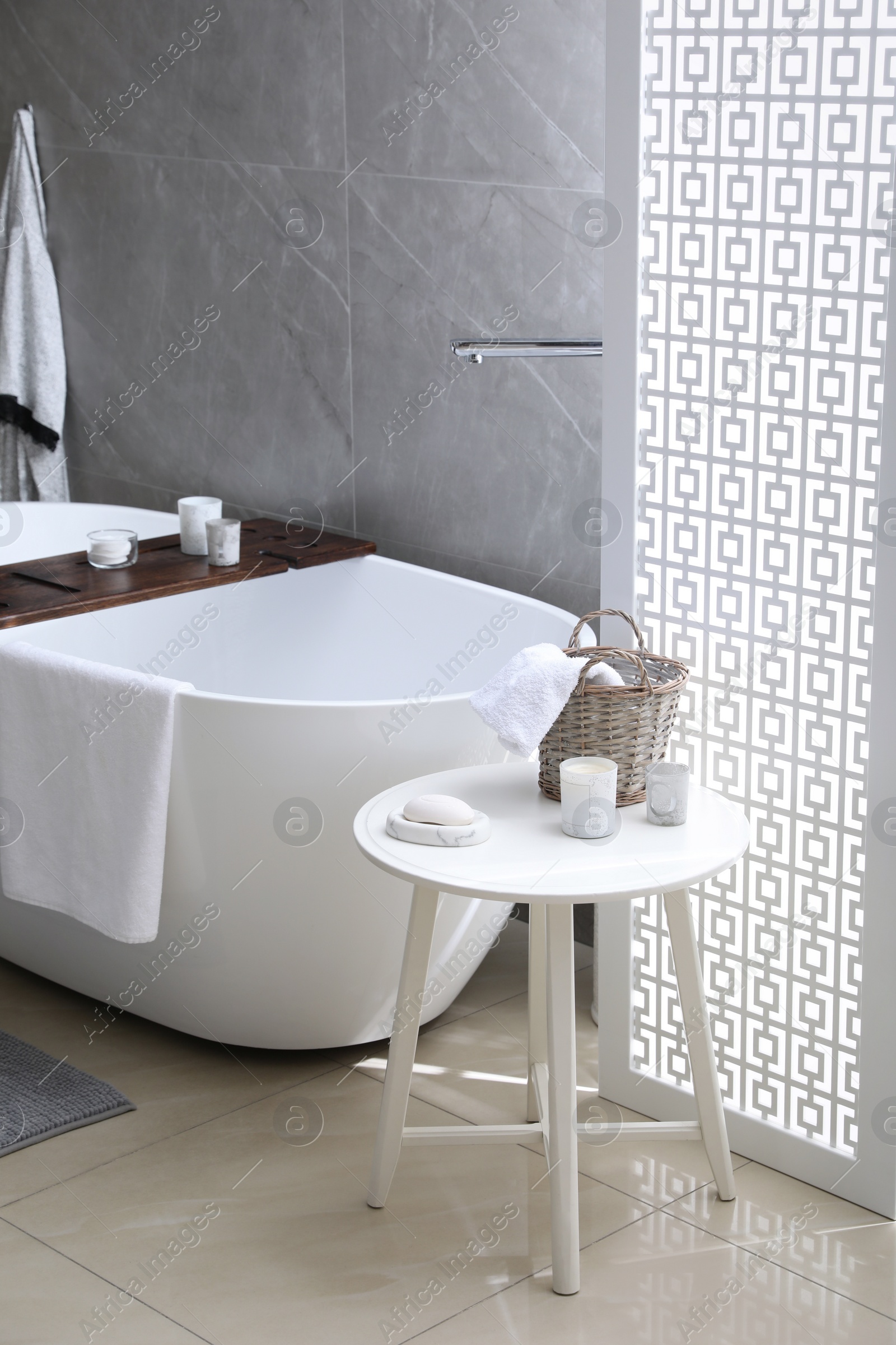 Photo of Modern white tub and table with toiletries in bathroom. Interior design