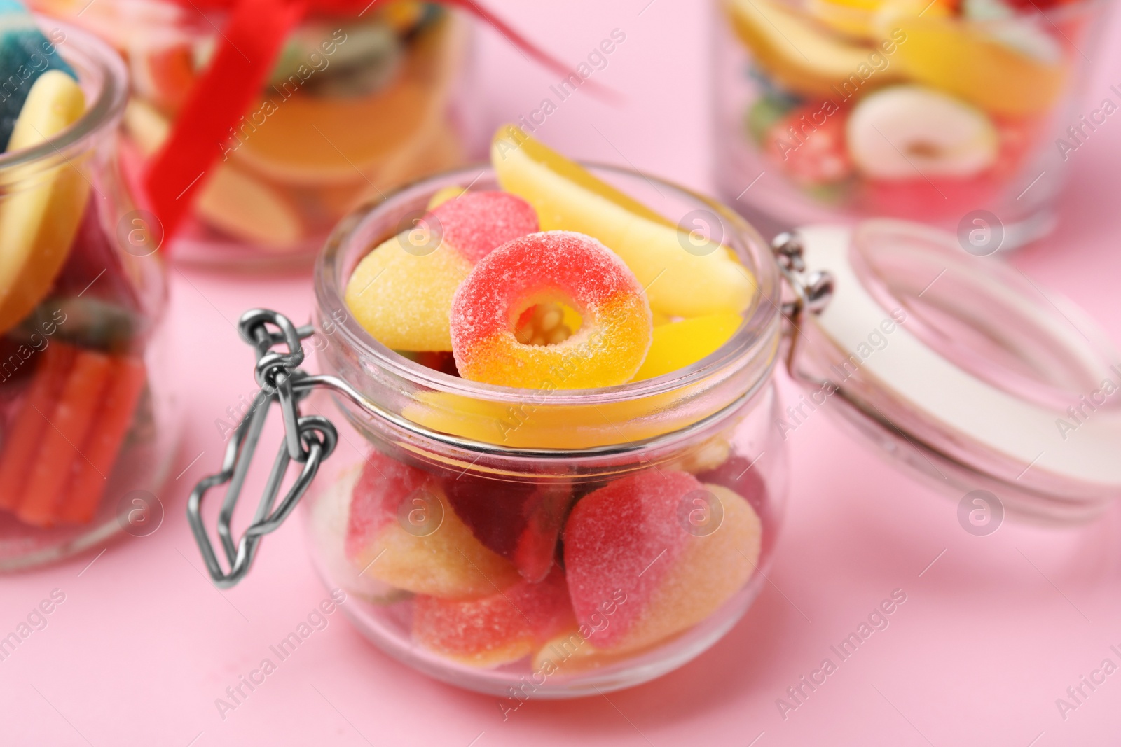 Photo of Glass jars with tasty colorful jelly candies on pink background, closeup